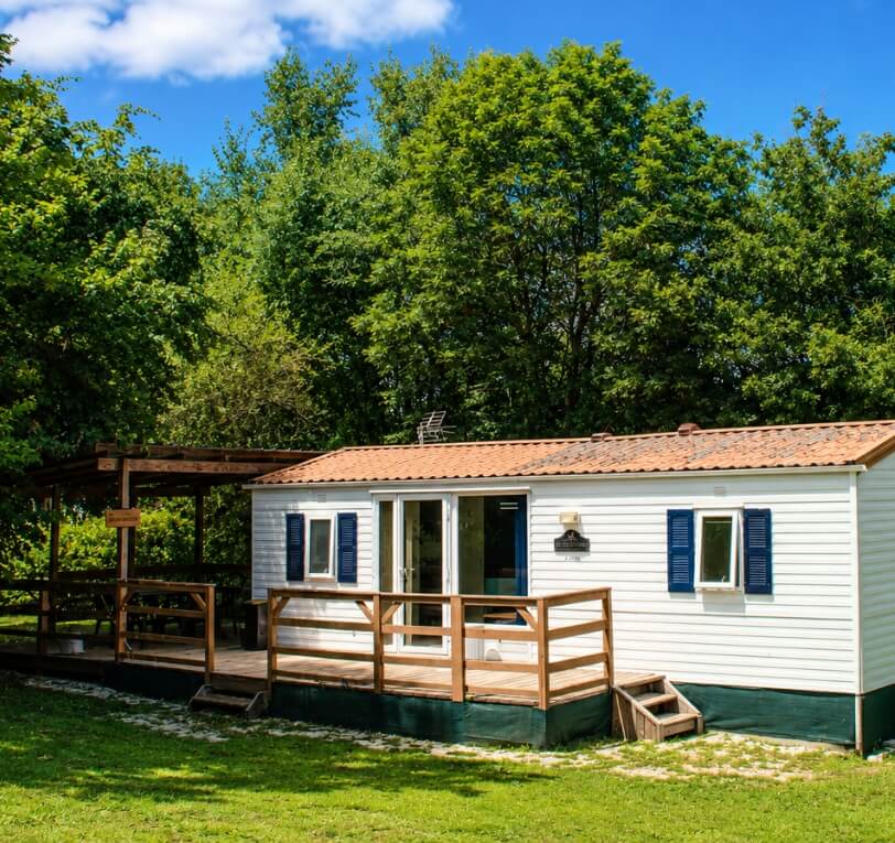 Exterior view of the mobile homes ‘Le Truffier’, ‘Le Cornouiller’, ‘Le Noisetier’ and ‘L’Olivier’, available to rent at Le Bel Air campsite in the Lot, featuring a wooden terrace