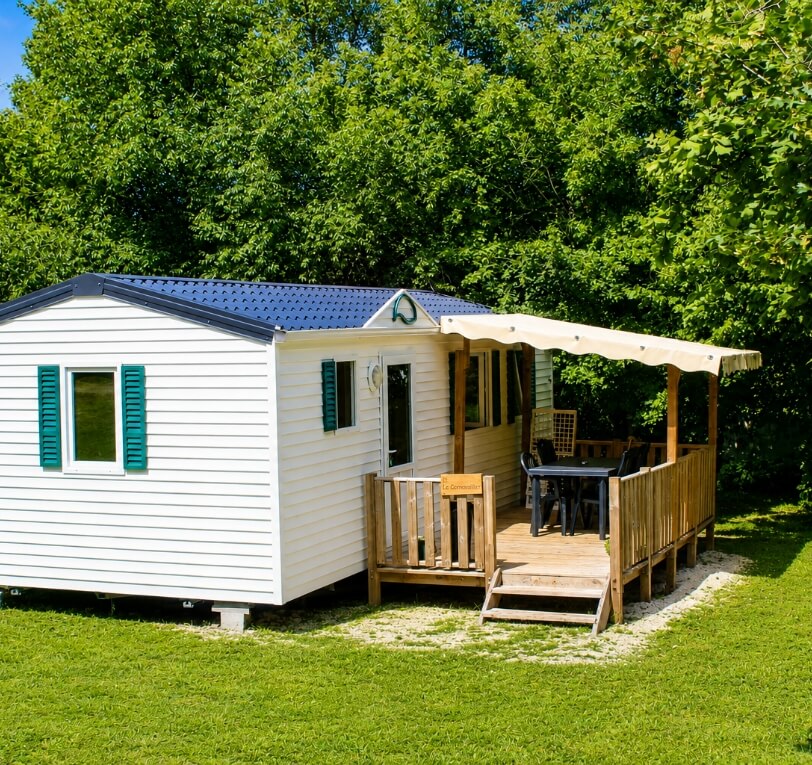 Exterior view of the ‘Le Truffier’, ‘Le Cornouiller’, ‘Le Noisetier’ and ‘L’Olivier’ mobile homes available for hire at Le Bel Air campsite in the Lot, featuring a semi-covered wooden terrace