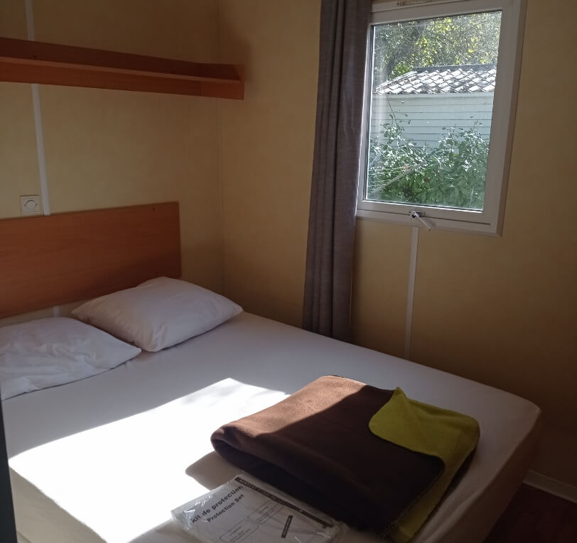 Bedroom with a double bed in the ‘Le Truffier’, ‘Le Cornouiller’, ‘Le Noisetier’ and ‘L’Olivier’ mobile homes available to rent at Le Bel Air campsite in the Lot