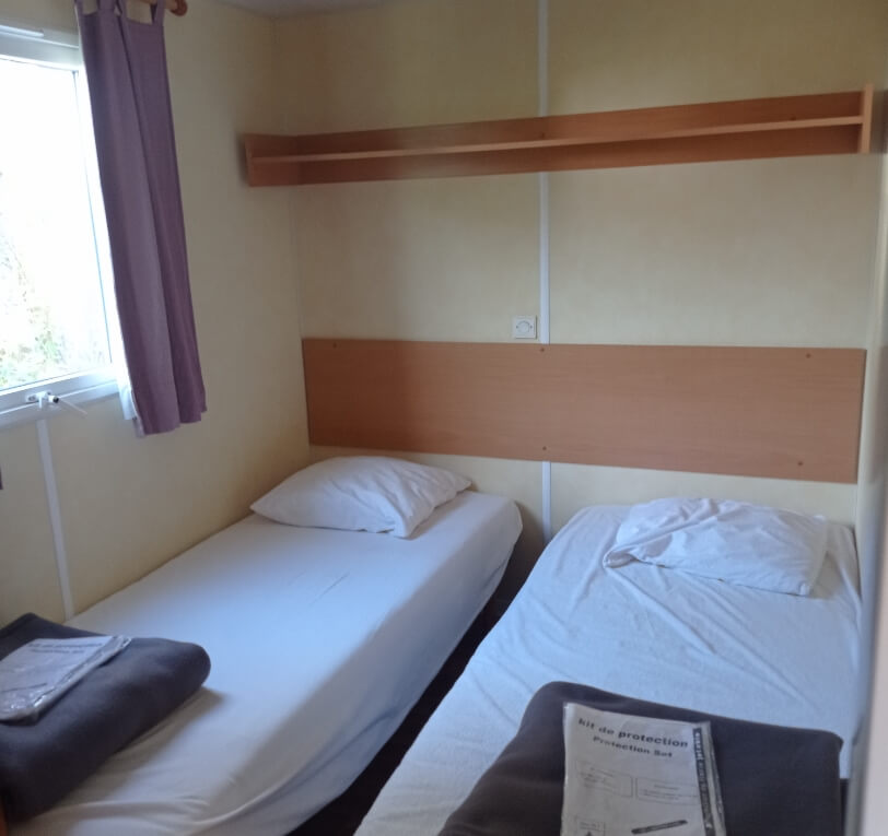 Bedroom with two single beds in the ‘Le Truffier’, ‘Le Cornouiller’, ‘Le Noisetier’ and ‘L’Olivier’ mobile homes available to rent at Le Bel Air campsite in the Lot